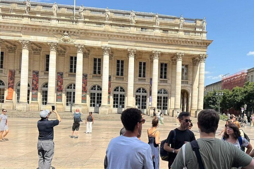 A historic building with columns and statues, people taking photos, and a clear sky. 4