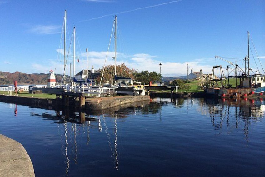 A calm harbor with several boats docked, a lighthouse in the background, and a clear sky. 3