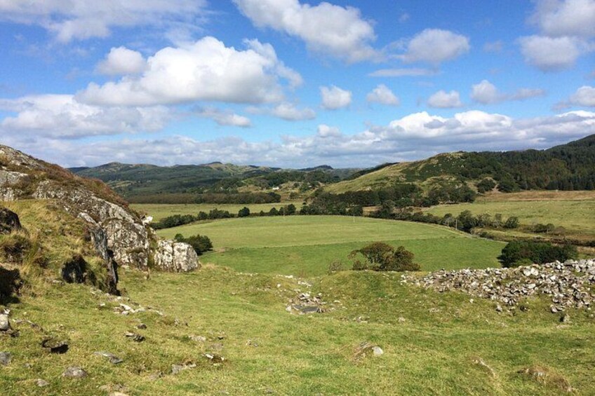 A grassy field with a stone wall and rolling hills in the background. 5