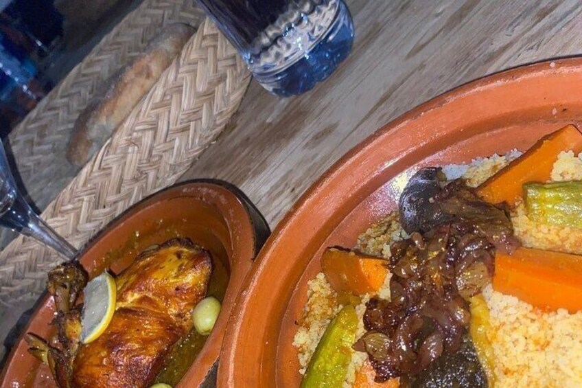 A meal with a roasted chicken leg, vegetables, and couscous in a clay pot. 4