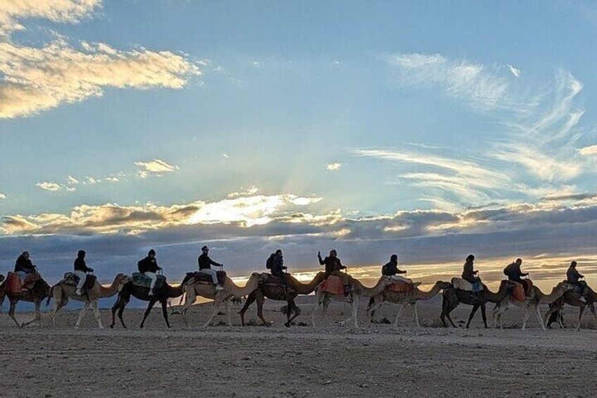 A group of people riding camels across a desert landscape during sunset. 2