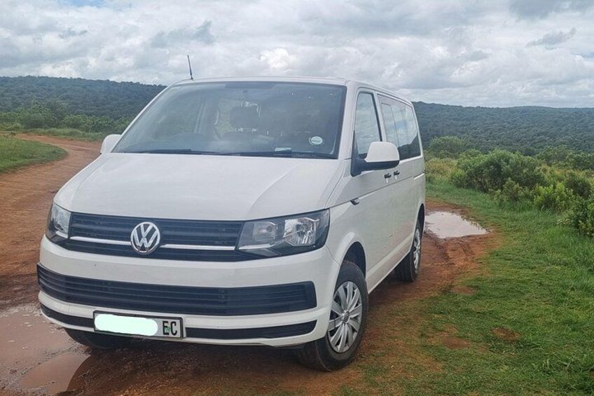 A white Volkswagen van parked on a dirt path with a green landscape in the background. 2