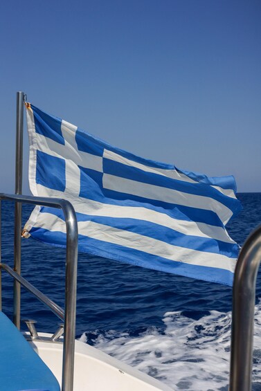 A flag on a boat with a metal railing and the ocean in the background. 1
