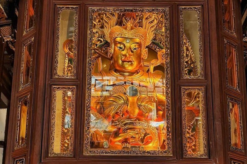 Een gouden Boeddhabeeld met ingewikkelde gravures en een serene uitdrukking, omgeven door versierde houten panelen. 2