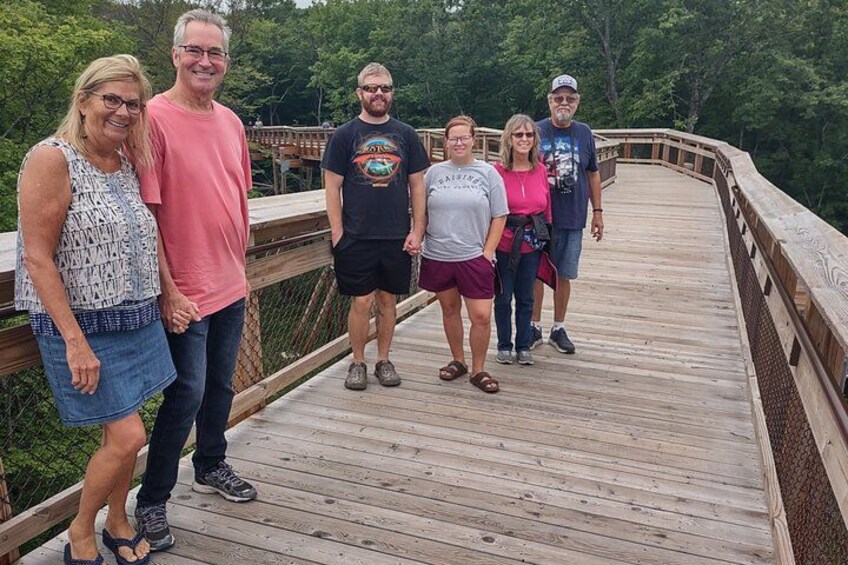A group of people standing on a wooden bridge surrounded by trees. 2