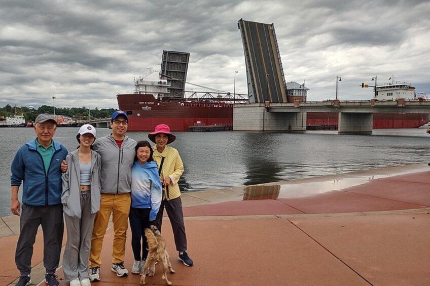 A group of people standing by a waterfront with a large ship and a bridge in the background. 4