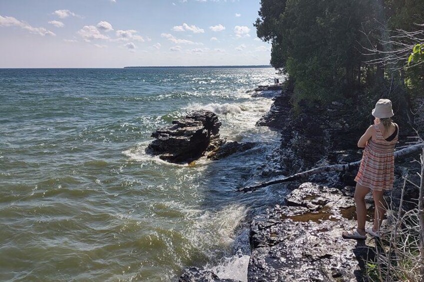 A person standing on a rocky shoreline by the sea, with waves crashing against the rocks. 3