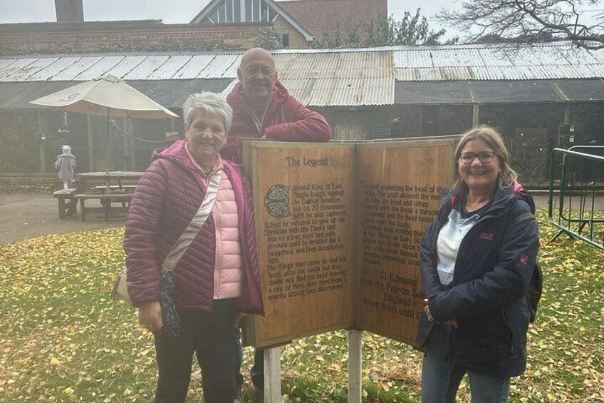 Three people standing in front of a wooden sign with text. 2