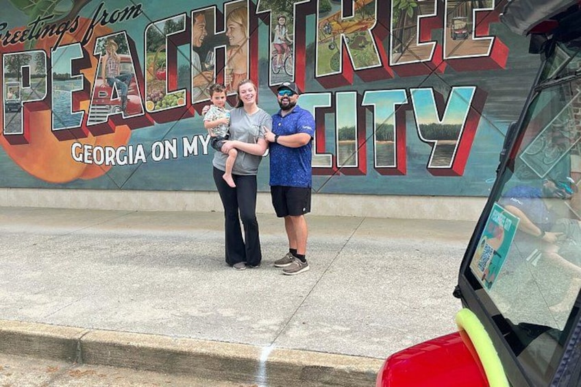 A mural with the words 'Greetings from Peach Tree City, Georgia' and a red vehicle in the foreground. 5