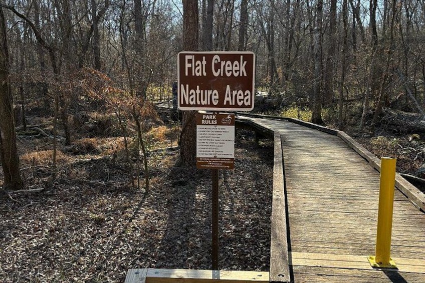 A wooden boardwalk leading into a forested area with a sign indicating Flat Creek Nature Area. 4