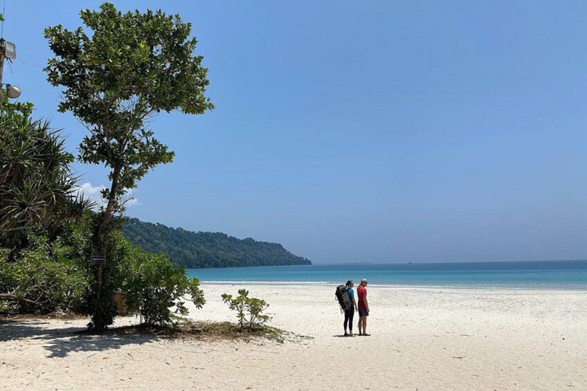 A beach with two people standing, a tree, and a distant shoreline. 5
