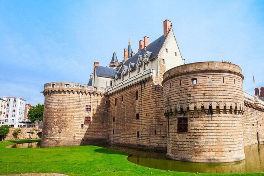 A historic castle with a moat, a grassy foreground, and a clear sky. 5