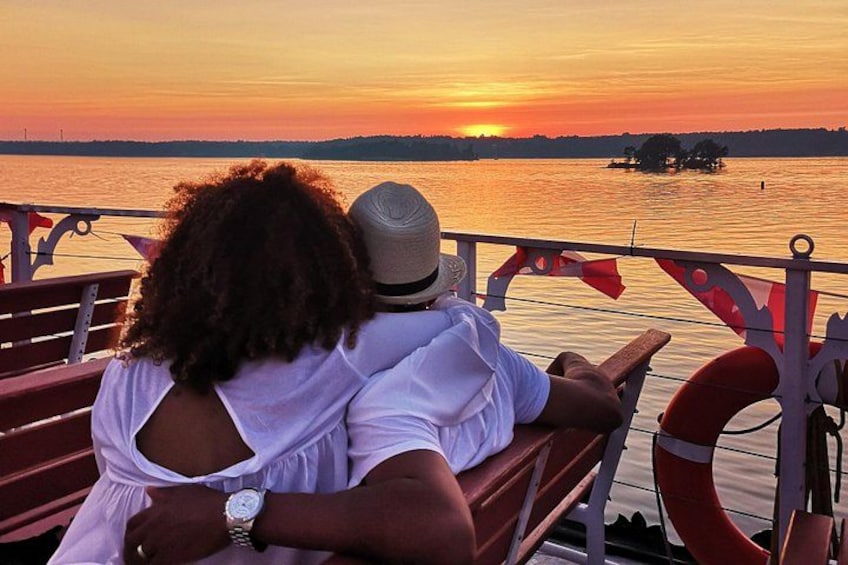Two people sitting on a bench overlooking a sunset over a body of water. 2