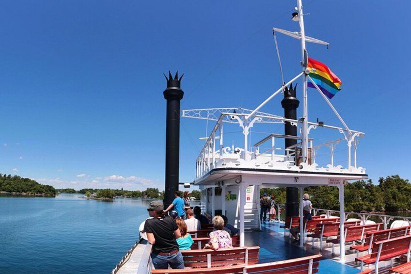 A boat with a black smokestack and a rainbow flag, passengers on deck, and calm water. 4