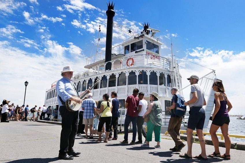 A steamboat with a person playing a banjo, people standing on the dock, and a clear blue sky. 5