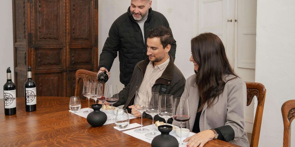A group of people seated at a wooden table with wine glasses and bottles. 4