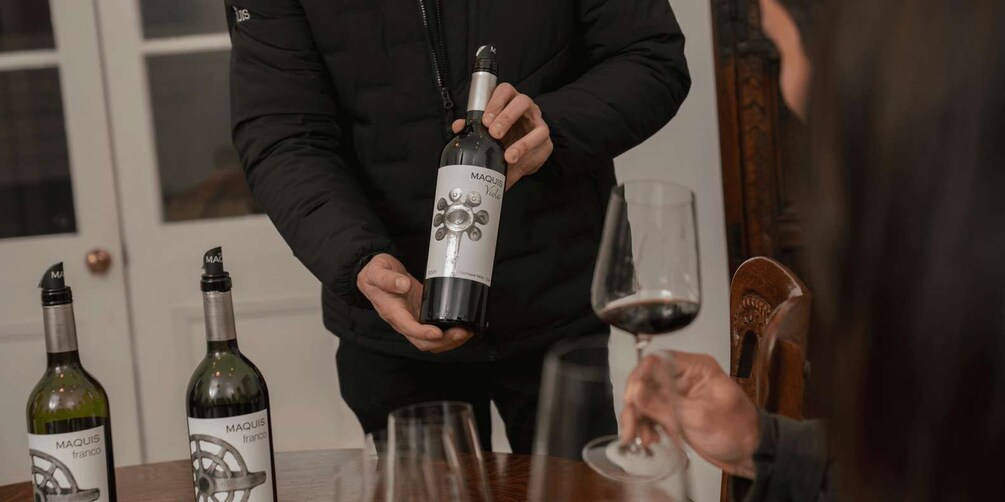A person holding a wine bottle with a label that reads 'MAQUIS franco.' 3