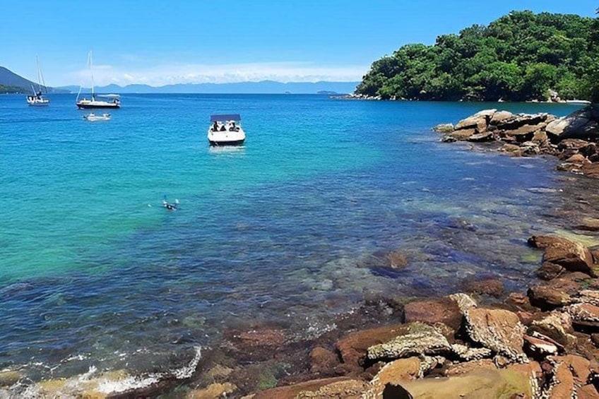 Mare azzurro e limpido con barche, costa rocciosa e un'isola boscosa. 4