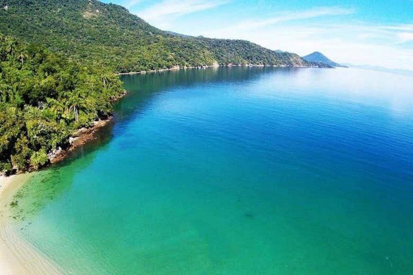 Paesaggio costiero con un mare blu cristallino, una spiaggia sabbiosa e un pendio boscoso. 5