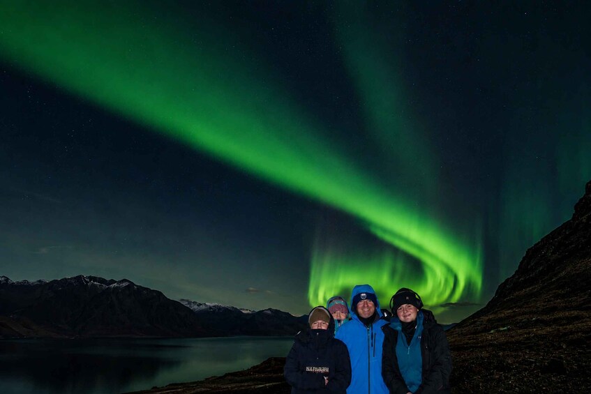 A group of people standing by a lake with the Northern Lights in the background. 4