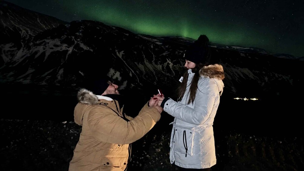 Two people outdoors at night with a mountain in the background and the Northern Lights in the sky. 2