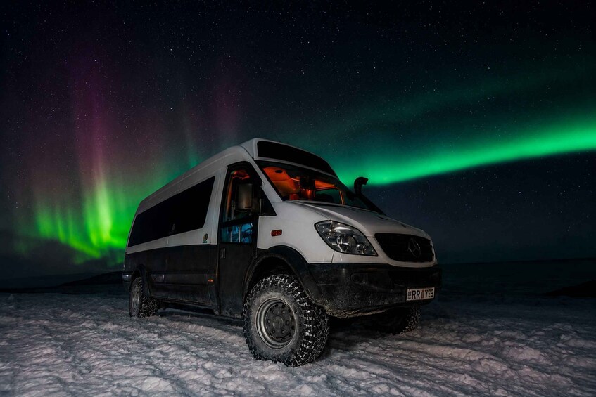 A white SUV parked on snow with the Northern Lights in the background. 3