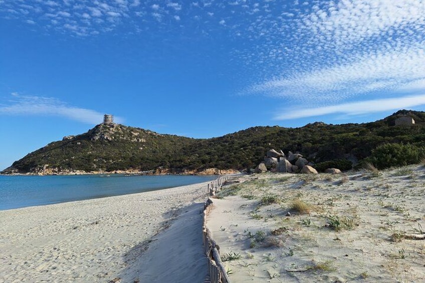 Una playa con un sendero que lleva a una estructura en la cima de una colina, un cielo azul despejado y un mar tranquilo. 2