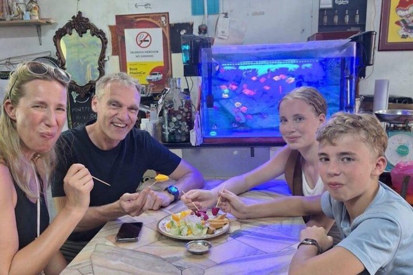 Four people sitting at a table with a plate of food and a fish tank in the background. 3