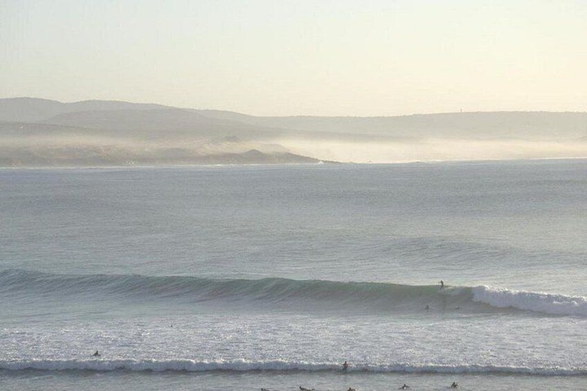 A beach with waves, a surfer, and distant mountains. 4
