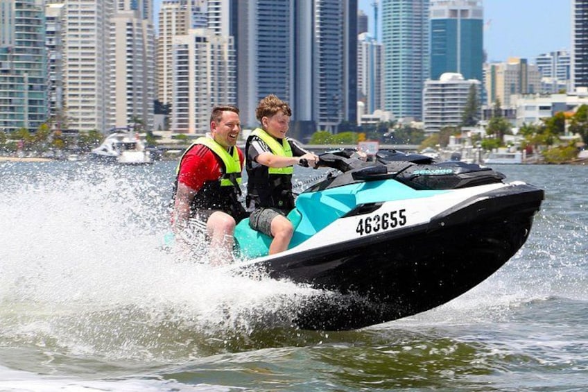 Two people on a jet ski with a city skyline in the background. 1