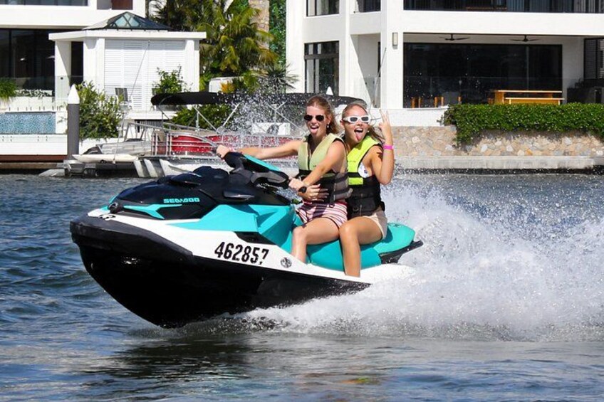 A jet ski with two people riding it, water splashing around, and a building in the background. 5
