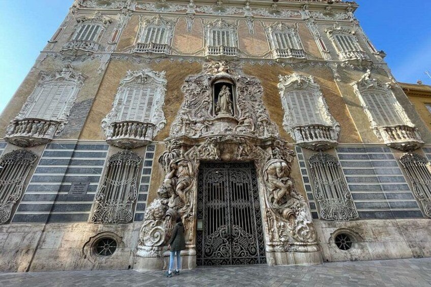 Een historisch gebouw met versierde decoraties, een grote centrale deur en meerdere ramen met ingewikkelde ontwerpen. 4