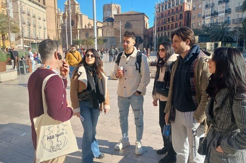 A group of people standing on a city square with buildings and a church in the background. 2