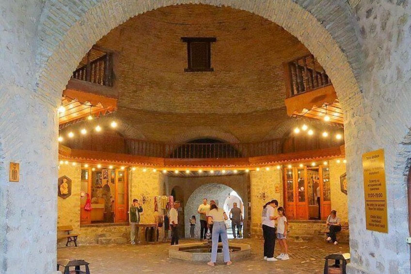 An arched stone structure with a central open space, surrounded by walls adorned with string lights and various artworks. 2