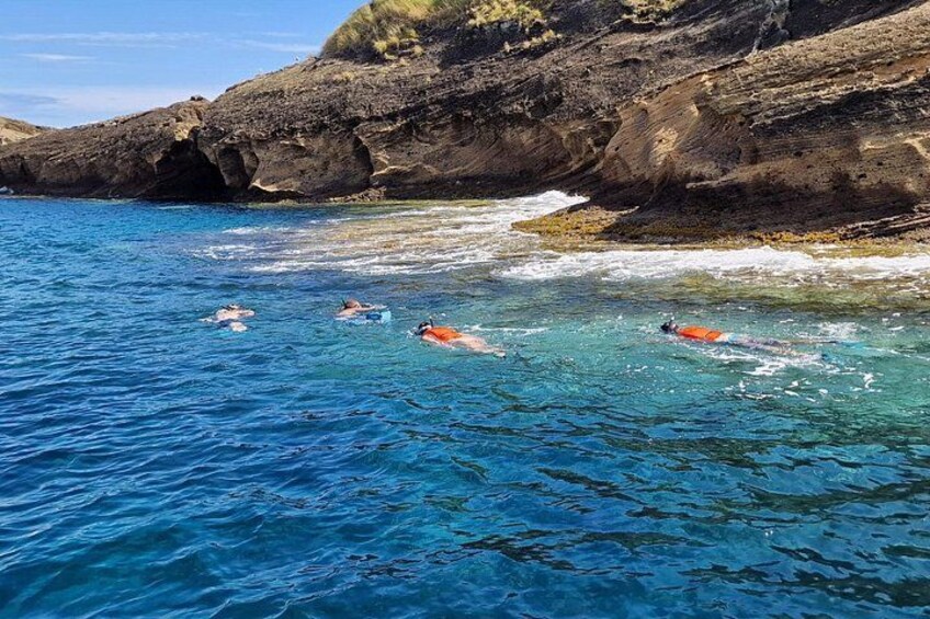 A coastal scene with clear blue water, rocky cliffs, and people swimming. 5