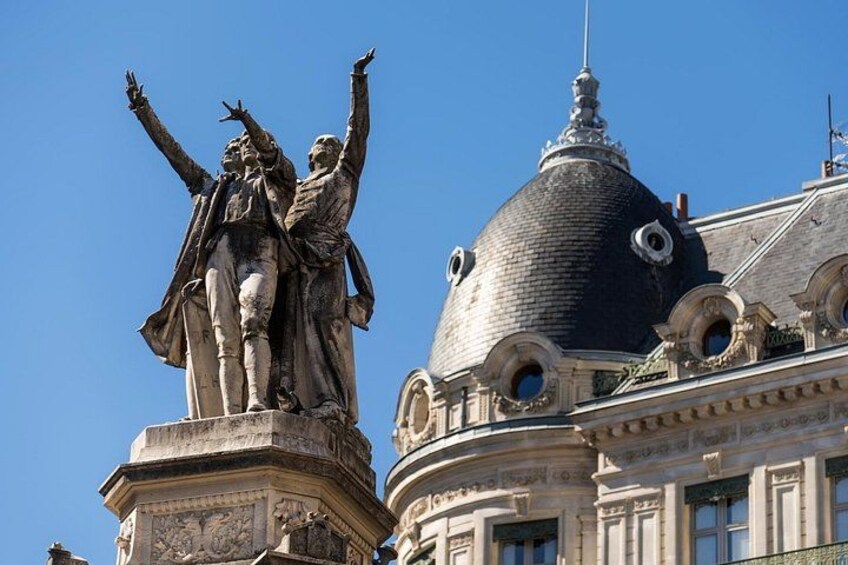 A historical statue with raised arms, a building with a dome, and classical architecture. 2