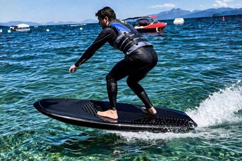 Una persona surfeando en un día despejado, con aguas tranquilas y barcos al fondo. 2