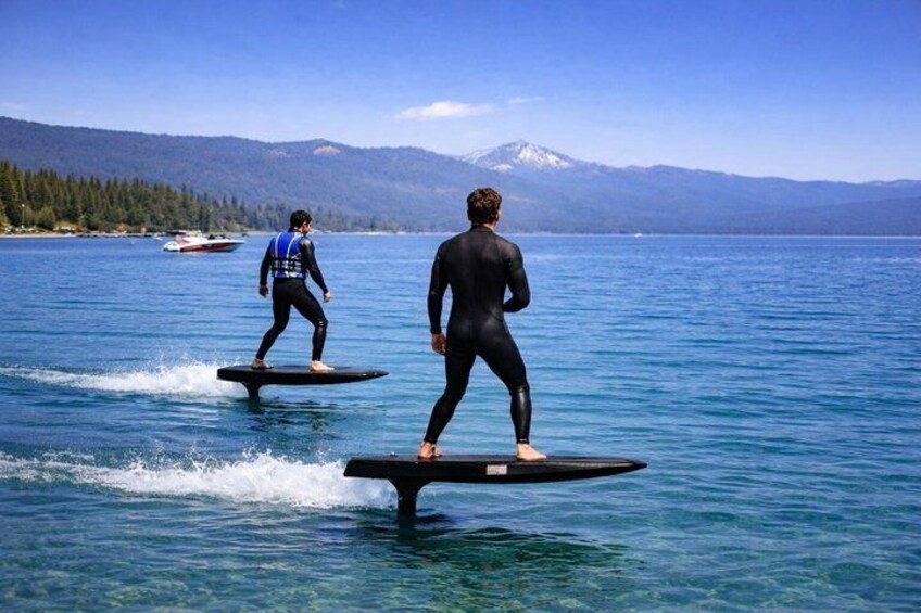 Dos personas practicando wakeboard en un lago, con montañas al fondo. 1