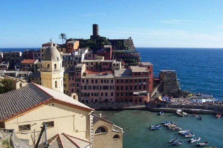 A coastal town with historic buildings, a prominent tower, and a fortified structure overlooking the sea. 3