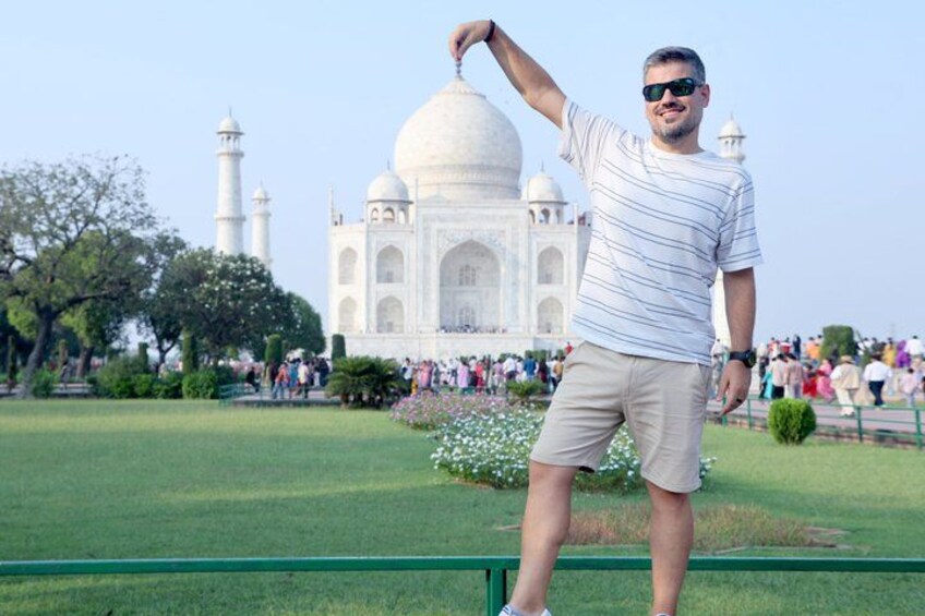 Eine Person steht vor dem Taj Mahal mit freier Sicht auf das berühmte, weiße Marmor-Mausoleum und seine vier Minarette. 2