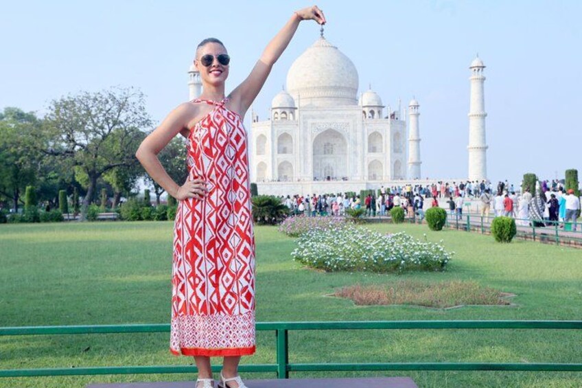 Eine Person in einem gemusterten Kleid vor dem Taj Mahal, mit freiem Blick auf das berühmte, weiße Marmor-Mausoleum und seine vier Minarette. 5