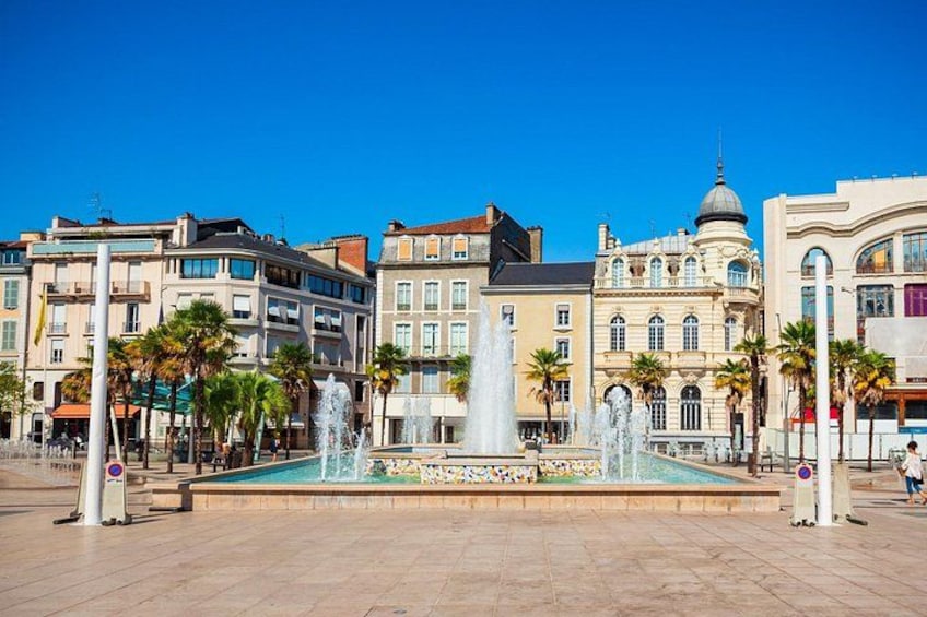 Une place publique avec une fontaine centrale, entourée de palmiers et de bâtiments historiques. 3