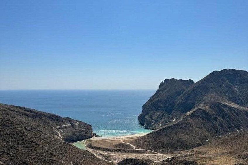 A coastal landscape with a clear sky, a beach, and rugged mountains. 1