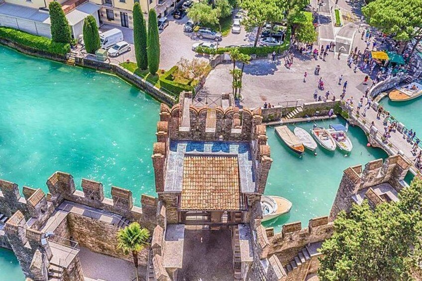 A historic stone bridge over a turquoise river, surrounded by lush greenery and a bustling waterfront area with boats and people. 3