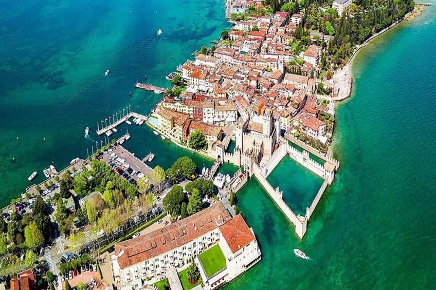 An aerial view of a coastal town with a fortified castle, a marina, and clear turquoise waters. 2
