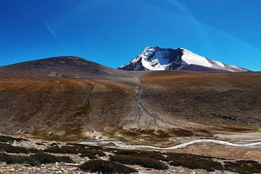 A mountainous landscape with a snow-capped peak, a winding path, and sparse vegetation. 2