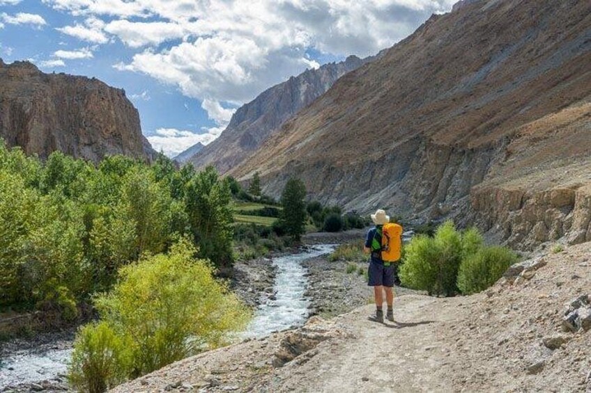 A hiker on a dirt path beside a river in a mountainous area. 2