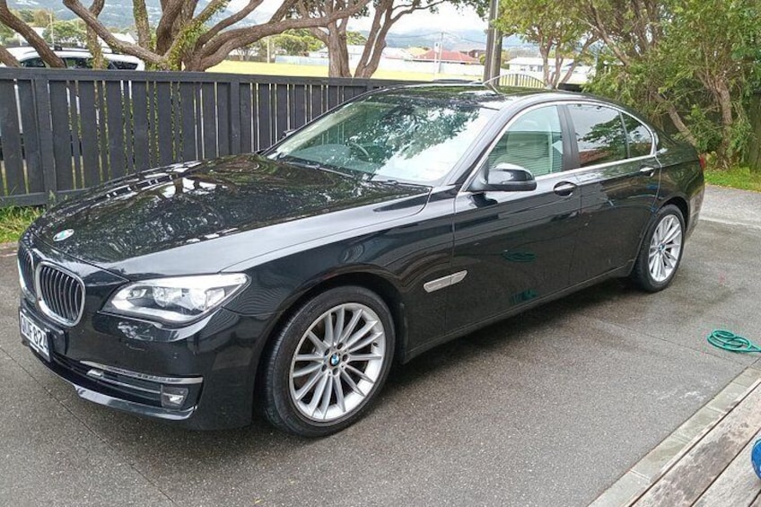 A black BMW sedan parked on a paved surface with a wooden fence and trees in the background. 3