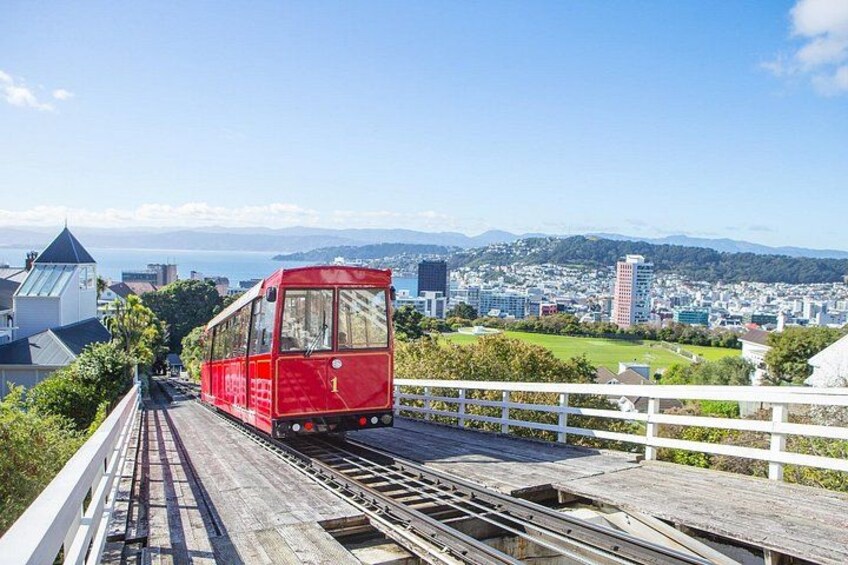 A red tram on a wooden bridge with a cityscape in the background. 2