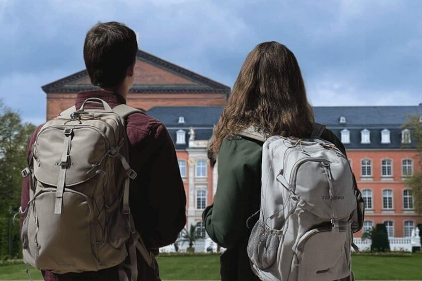Deux personnes, portant des sacs à dos, se tiennent devant un grand bâtiment doté d’un toit rouge et de colonnes. 2